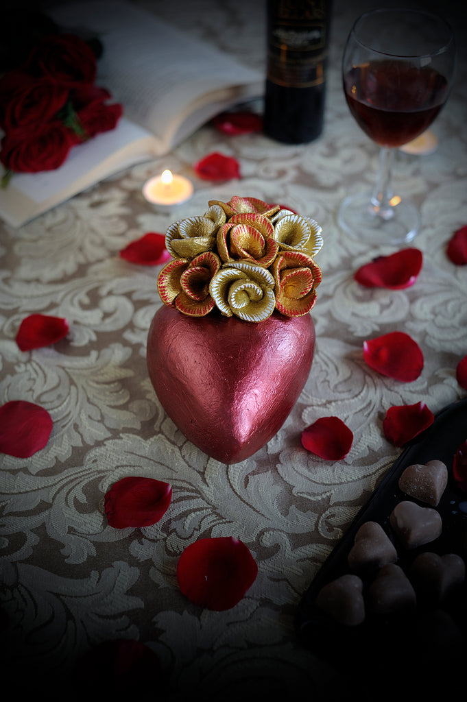 Hand-made clay heart, painted in metallic red giving the illusion of a heart shaped chocolate wrapped in red foil. On top it is beautifully decorated with a bouquet of roses painted in metallic gold. This stunning heart decoration can also be hung on a wall. All our catrinas and hearts are made in Mexico and we ship worldwide. Add a classy touch of Mexican art to your home.