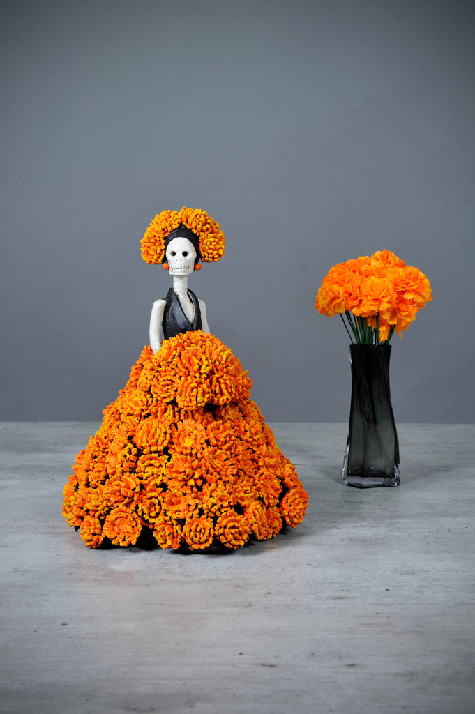 Hand-made clay figurine.Catrina Gisela is a unique Catrina, wearing a stunning ball gown covered in cempasúchil(Marigold) flowers. This type of flower is an important piece used to decorate Day of the Dead altars.  Each flower is hand-made and painted before carefully placing it on her dress. Gisela is the perfect addition to your Day of the Dead altar.  All of our Catrinas are made in Mexico and we ship worldwide. Add a classy touch of Mexican culture to your home.