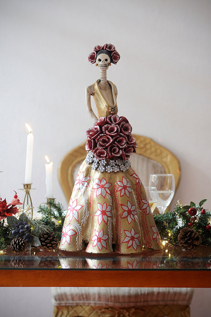 Hand-made clay figurine, Catrina Fernanda is ready for the Christmas party, she is wearing a beautiful gold dress, decorated with hand-painted poinsettias and small silver flowers around her bouquet of roses. She is also wearing a beautiful headpiece. Add a classy touch of Mexican art to your home or office. All our Catrinas are made in Mexico and shipped worldwide.