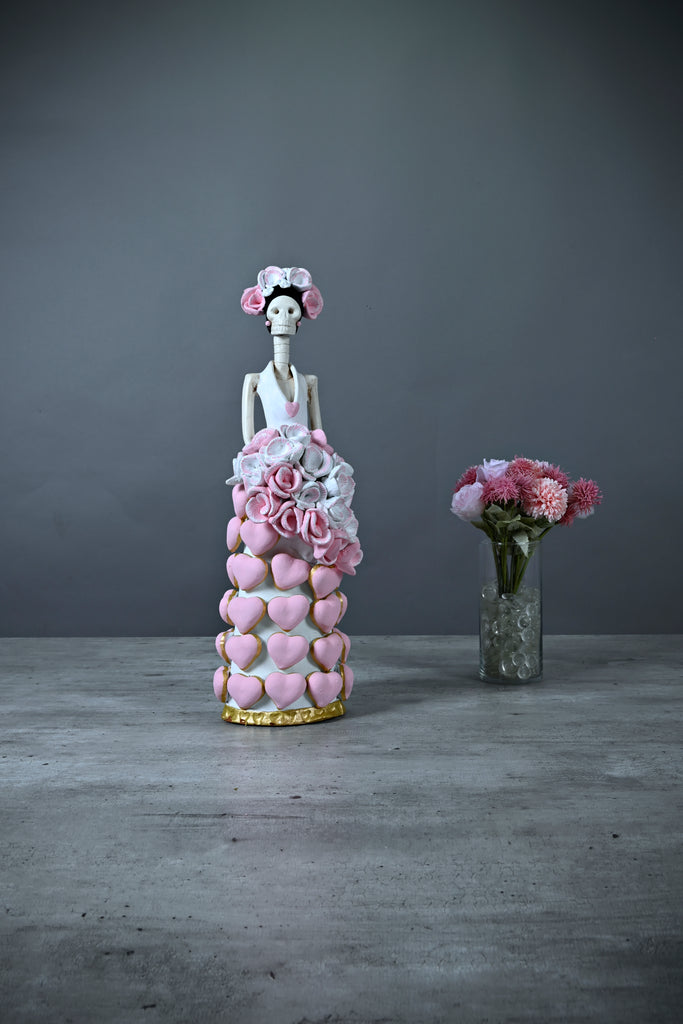 Catrina Isabela is part of our Valentine's Day Catrina collection.  She is wearing a fantastic white dress with pink hand-made hearts. We decided to give her a bouquet of pink and white flowers to match her beautiful headpiece. At the bottom, the dress is lined with gold detailing.  If you are looking for the perfect Valentine's Day gift, consider getting a Catrina, these beauties last forever and will look amazing in any room in your house!