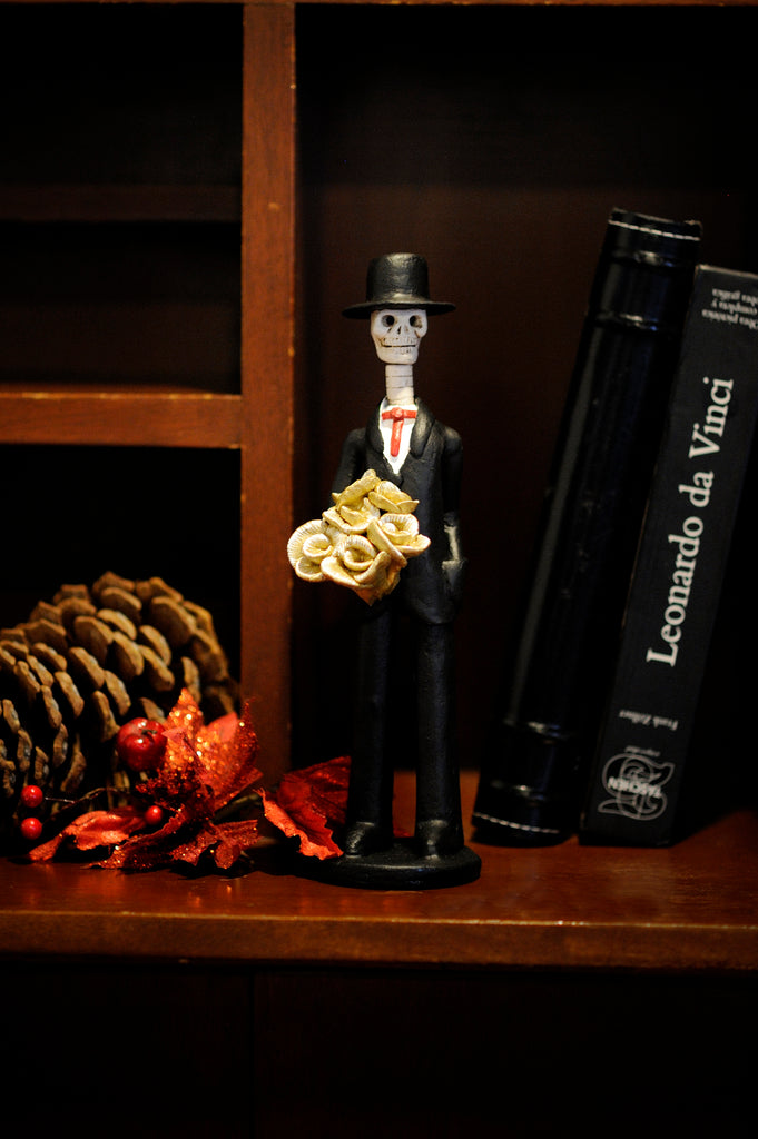 Hand-made clay figurine, our Catrin Diego is wearing a black suit with a red bowtie and holding a yellow rose bouquet for his date. All our Catrines and Catrinas are made in Mexico, we ship worldwide. Add a classy touch of Mexican art to your home. 