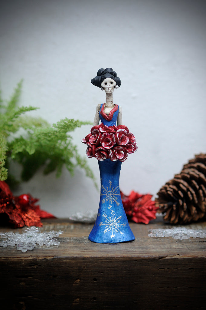Hand-made clay figurine, Cynthia is wearing a curve-skimming blue dress with silver details on her dress.She is holding a red rose bouquet. All our Catrinas are made in Mexico and shipped worldwide. Add a classy touch of Mexican culture to your home. 