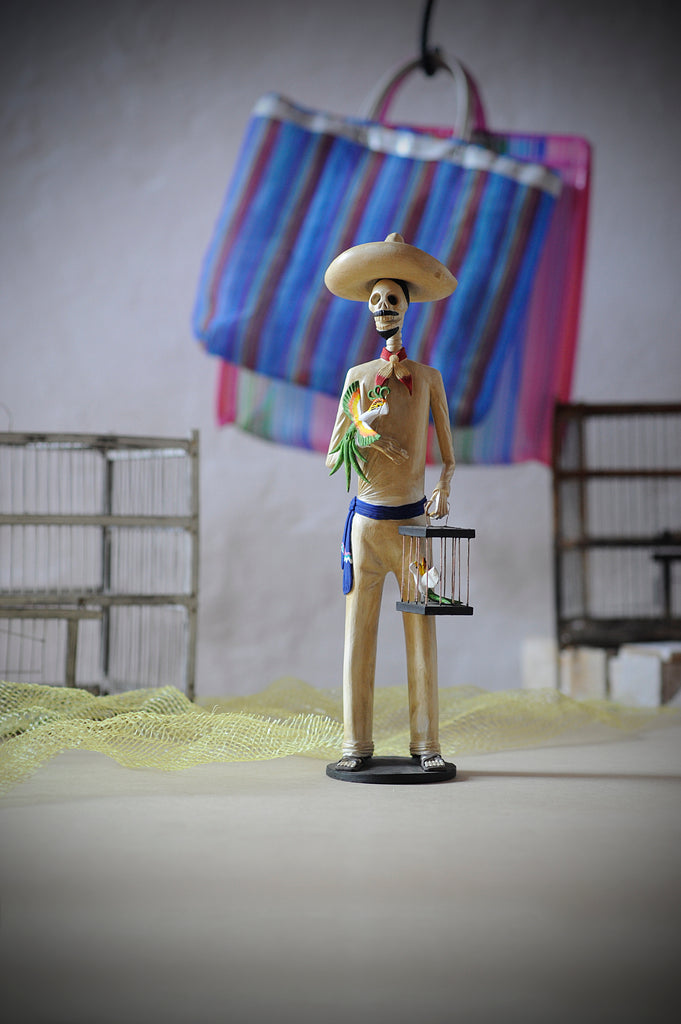 Hand-made clay figurine, Catrin Horacio is wearing a simple beige outfit with a blue belt and he is holding bird sculptures that have incredible detail. He ie s part of the El Mercado Collection. All our Catrines and Catrinas are made in Mexico and we ship worldwide. Add a classy touch of Mexican art to your home.