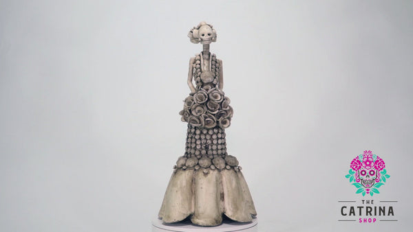 Hand-made clay figurine, Catrina Victoria is a stunning art piece. The artist gave her a beautiful dress with rosebuds all over the dress, and at the bottom some ruffled layers. All our Catrinas are made in Mexico and we ship worldwide. Add a classy touch of Mexican culture to your home.