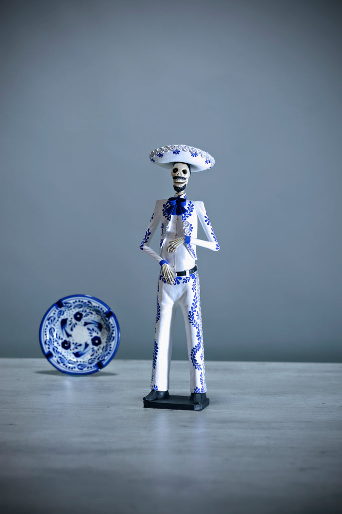 Hand-made clay figurine. Catrin Javier in white is a handsome guy, wearing a crisp white charro suit with an intricate design in blue that matches his bowtie. Take a close look and admire the beautiful details throughout the suit and hat. All of our catrinas are made in Mexico and we ship worldwide. Add a classy touch of Mexican art to your home.