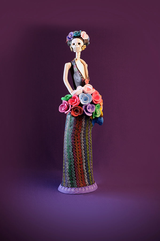 Hand-made clay figurine, Alejandra is wearing a plunging neckline with a dotted pattern A-line skirt. She has a colorful bouquet of roses and she is also wearing a roses headpiece. Add a touch of Mexican art to your home. We ship worldwide