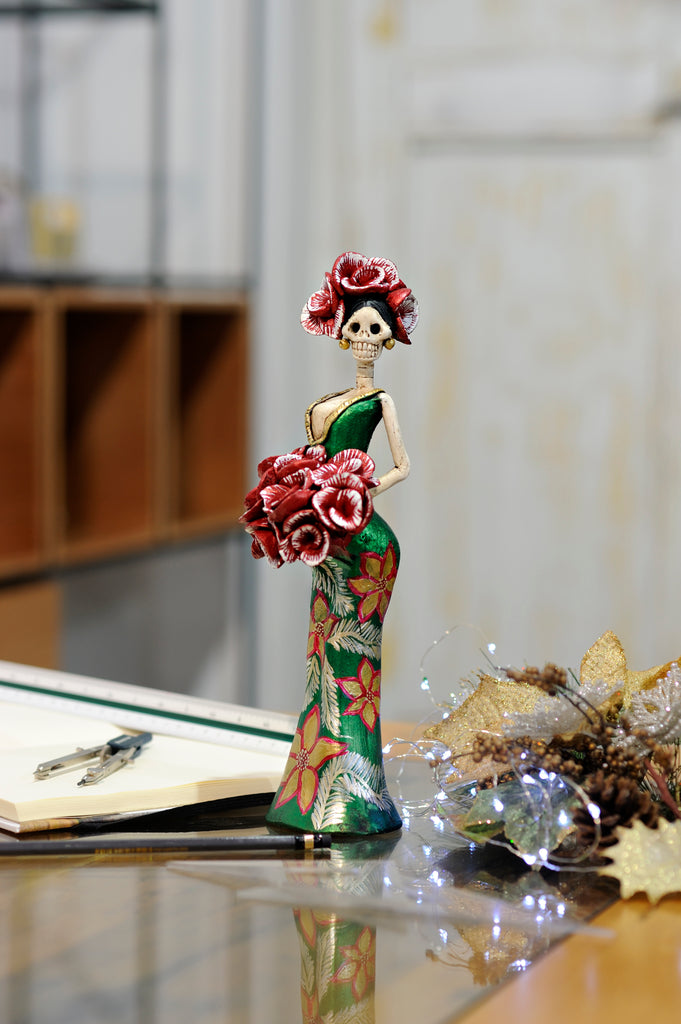 Catrina Cynthia Christmas Green is a hand-made clay figurine, Cynthia is wearing a curve-skimming green dress with gold poinsettias on her dress.She is holding a red rose bouquet. All our Catrinas are made in Mexico and shipped worldwide. Add a classy touch of Mexican culture to your home. 