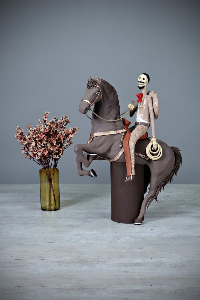 Catrin Julian is a handsome charro wearing a light brown suit with incredible gold detailing. Julian is riding on his noble steed Rayo, which is a beautifully made horse painted in brown with gold detailing as well. This stunning piece of art will look amazing in your home! Add a classy touch of Mexican art to your home.