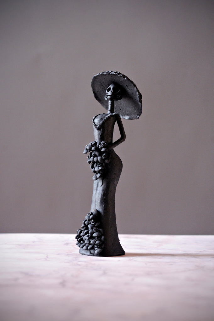 Hand-made clay figurine, Catrina Catalina in black is stunning. She is wearing a form fitting dress that accentuates her figure, and a stunning hat to add style to her already impressive outfit. All our Catrinas are made in Mexico and we ship worldwide. Add a classy touch of Mexican culture to your home.