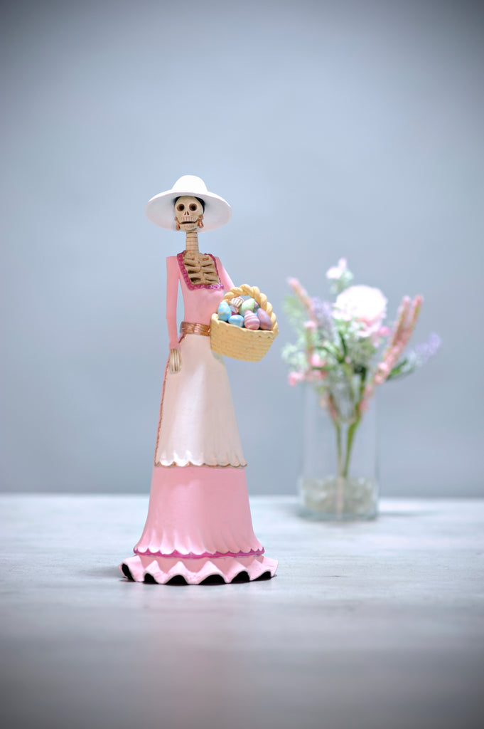 Hand-made clay figurine, Catrina Clarisa is part of our Easter collection. Clarisa is wearing a beautiful pastel pink dress and a white apron with small ruffling at the bottom. She is also wearing a cute white hat and she is holding a gorgeous Easter egg basket filled with colorful eggs. All our Catrinas are made in Mexico and we ship worldwide. Add a classy touch of Mexican culture to your home.