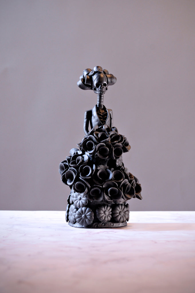 Hand-made clay figurine, Catrina Martina is painted in black, she is wearing a black dress covered in flowers, but her bouquet is wrapped around her for added style. All our Catrinas are made in Mexico and we ship worldwide. Add a classy touch of Mexican culture to your home. 