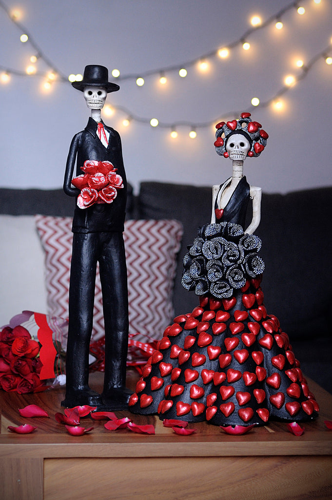 Hand-made clay figurines, Catrines Elena & Pablo are a beautiful couple designed for Valentine's Day. Elena is wearing a mermaid dress with hearts all around the skirt, she is holding a black rose bouquet and the artist added the same hearts to her headpiece. Pablo is a tall Catrin that complements our tall Catrinas. He is wearing a black tux with a red tie and a red rose bouquet. All our Catrinas are made in Mexico and we ship worldwide. Add a classy touch of Mexican art to your home. 