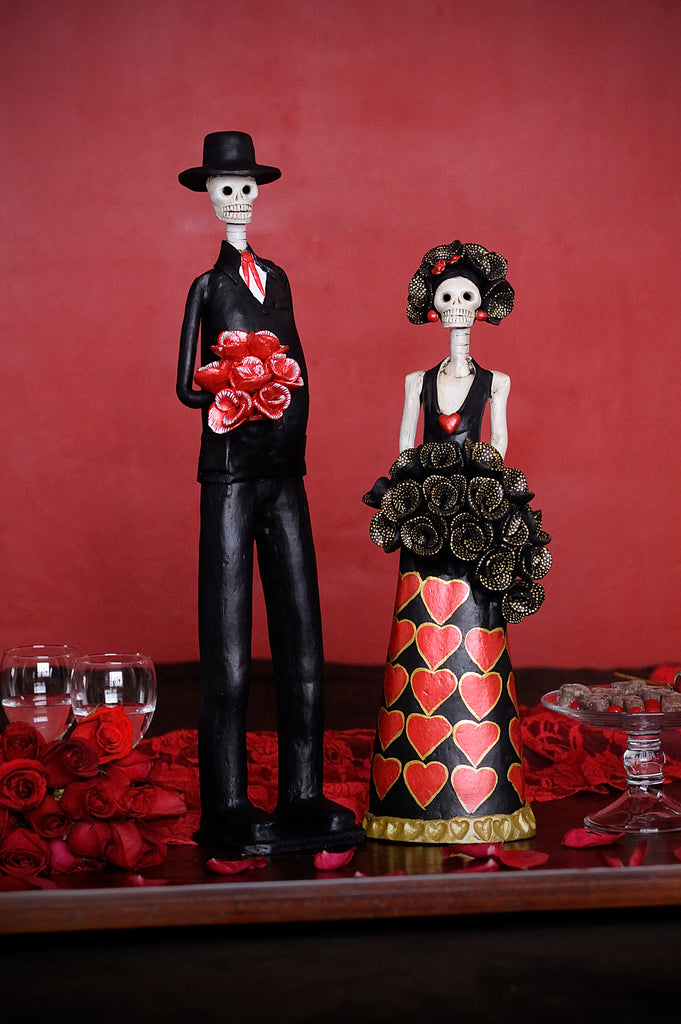 Hand-made clay figurines, Catrines Olivia and Pablo are a beautiful couple designed for Valentine's Day. Olivia is wearing a beautiful black dress with hand-painted hearts and a black rose bouquet that makes her whole outfit standout. Pablo is one of our tall Catrines designed to accompany any tall Catrina; he is wearing a black tux with a red tie and a red rose bouquet. All our Catrinas are made in Mexico and we ship worldwide. Add a classy touch of Mexican culture to your home.