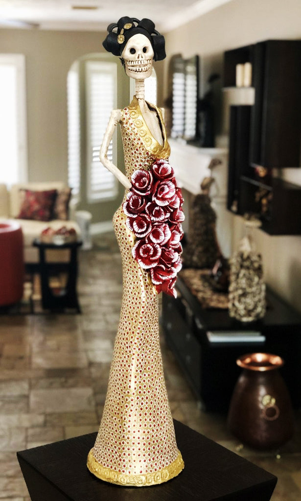Hand-made clay figurine, Estela in gold is one of our tallest Catrinas. She is wearing a sleek trumpet style dress, with a deep neckline. Her stunning dress has a dotted flower design that makes her cascading bouquet stand-out even more. All our Catrinas are made in Mexico, we ship worldwide. Add a classy touch of Mexican art to your home or office. 