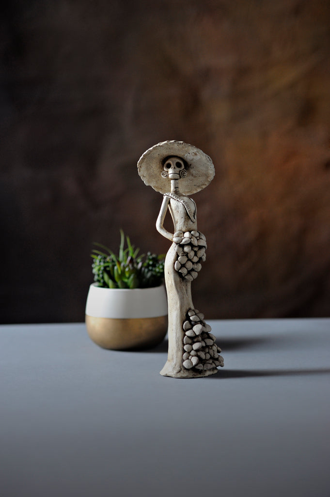 Catalina belongs to the small Catrina’s collection, but what’s wrong with being small when she is one of a kind!  Displaying a sexy mermaid dress, a creative design with pretty Forget me Not’s on the skirt and bouquet, our artist has created Catalina!    Catalina's hat makes her one of our most unique Catrinas. She will look stunning in your home or office. 