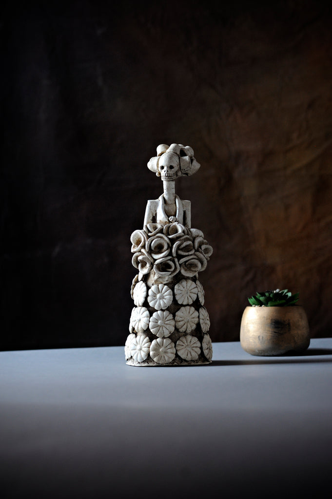 Hand-made clay figurine, Catrina Julia is wearing a cute dress covered in daisies, and to finish off her look, she is holding a rose bouquet. All our Catrinas are made in Mexico and we ship worldwide. Add a classy touch of Mexican culture to your home.