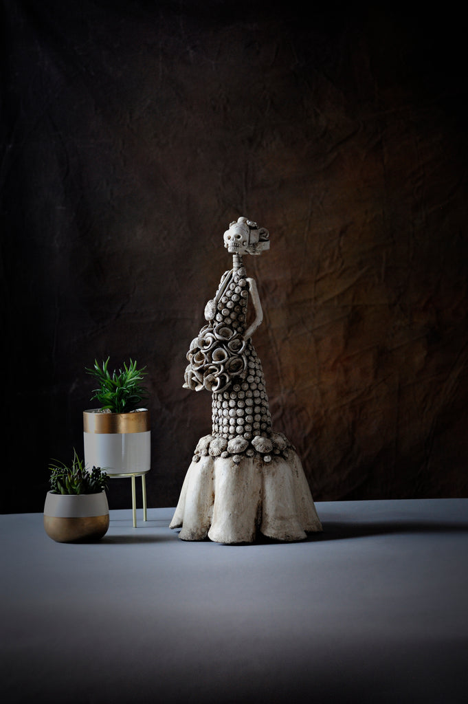 Hand-made clay figurine, Catrina Victoria is a stunning art piece. The artist gave her a beautiful dress with rosebuds all over the dress, and at the bottom some ruffled layers. All our Catrinas are made in Mexico and we ship worldwide. Add a classy touch of Mexican culture to your home.
