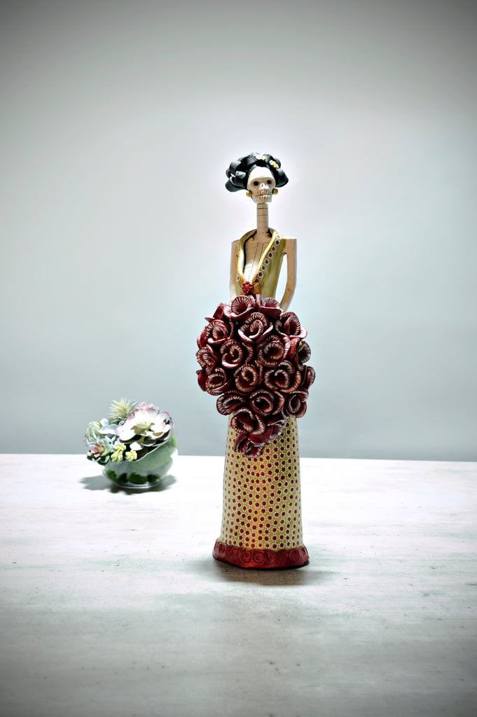 Hand-made clay figurine, Catrina Josefina Red Carpet in Gold is a stunning art piece. She is wearing a gold dress with a dotted pattern design. She is holding a cascading burgundy rose bouquet and to adorn her head, we added a few dainty flowers. All our Catrinas are made in Mexico and we ship worldwide. Add a classy touch of Mexican culture to your home.