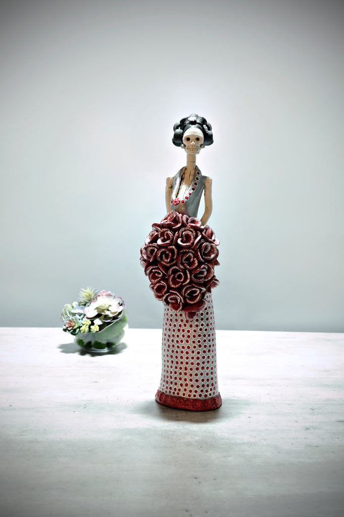 Hand-made clay figurine, Catrina Josefina Red Carpet in Silver is a stunning art piece. She is wearing a silver gown with a dotted pattern all over the skirt. The artist gave her a stunning cascading rose bouquet and to finish off her look, two small flowers on her hair. All our Catrinas are made in Mexico and we ship worldwide. Add a classy touch of Mexican culture to your home. 