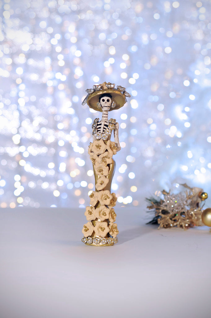 Catrina Samantha is wearing a beautiful gold dress with beige poinsettias added by hand.  Her European-style hat is the same color as her dress, with silver ornaments that match her earrings and the dress's neckline.   Samantha in gold is the smallest out of the three sisters; no matter which Catrina you choose, she will make a great addition to your home.