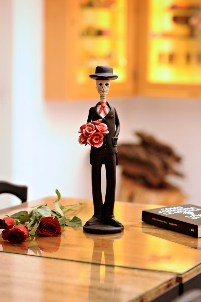 Hand-made clay figurine, Catrin Roberto is part of our Valentine's Day Collection. Roberto is wearing a fancy black suit with a red tie and a sleek hat. Roberto can complement any Catrina with red flowers. All our Catrines and Catrinas are made in Mexico and we ship worldwide. Add a classy touch of Mexican art to your home.
