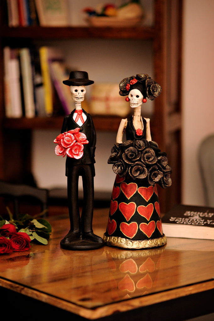 Hand-made clay figurines, Graciela and Roberto are part of our Valentine's Day collection. She is wearing a black dress with hand-painted hearts and a beautiful black rose bouquet, Roberto is wearing a black suit with a red tie, he is holding a flower bouquet for his sweetheart. All our Catrines and Catrinas are made in Mexico and we ship worldwide. Add a classy touch of Mexican culture to your home.