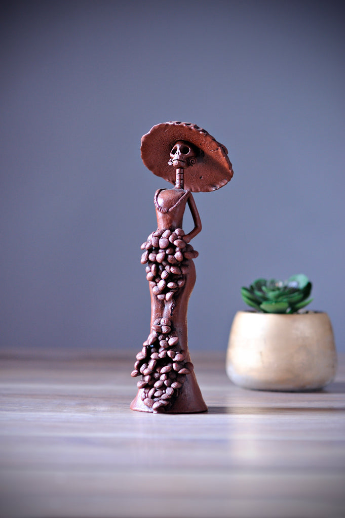 Catrina Catalina belongs to the small Catrina’s collection, but what’s wrong with being small when she is one of a kind?  Displaying a sexy mermaid dress, a creative design with pretty Forget Me Not’s on the skirt and bouquet, our artist has created Catalina, a unique piece of art, dressing her with the original Catrina Hat as Diego Rivera painted it. 
