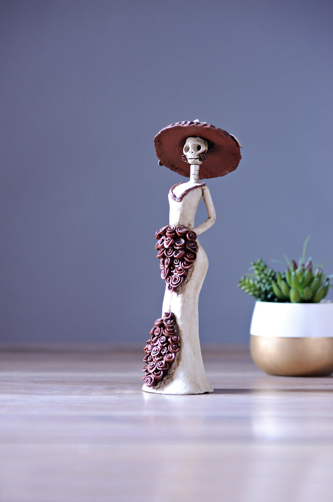 Catrina Catalina belongs to the small Catrina’s collection, but what’s wrong with being small when she is one of a kind?  Displaying a sexy mermaid dress, a creative design with pretty Forget Me Not's on the skirt and bouquet, our artist has created Catalina, a unique piece of art, dressing her with the original Catrina Hat as Diego Rivera painted it. 