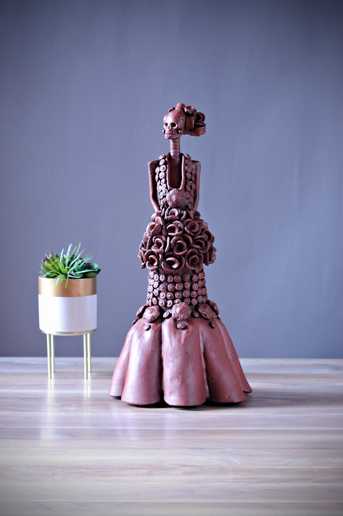 Victoria represents the classic refinement of what the great painter Diego Rivera envisioned of the Catrina. Classy, and feminine, Victoria is embodied in a magnificent dress with a sophisticated flower pattern, which unveils an impressive flower arrangement and a ruffled tapestry base, all combined to perfection!