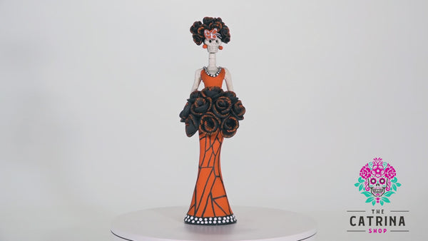 Hand-made clay Catrina; Catrina Monica is wearing a beautiful orange dress that resembles the wing of a Monarch butterfly, she is wearing a beautiful headpiece with black roses and splashes of orange. Her rose bouquet matches the hairpiece.
